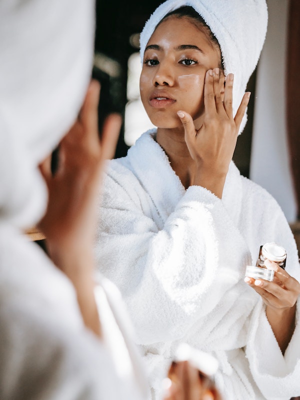 Black woman with towel applying cream on face
